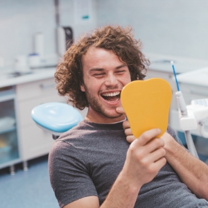 Young man in dental chair looking at his smile in a hand mirror