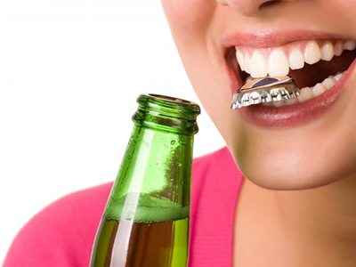 Close up of woman using her teeth as a bottle opener