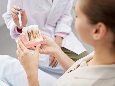 Dentist pointing to a model of dental implants and instructing her patient