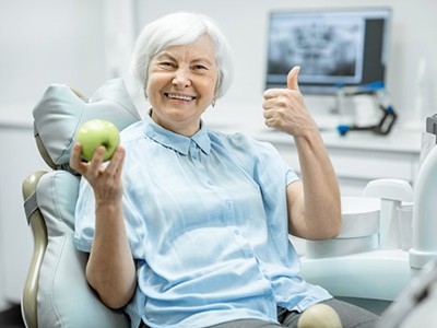 Senior woman sitting in the patient chair holding an apple