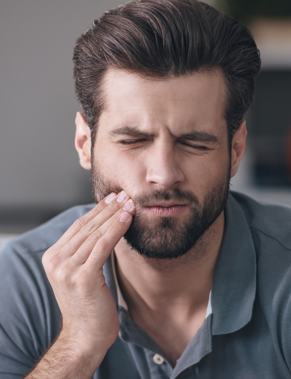 Man holding his cheek and wincing in pain before root canal treatment in Succasunna