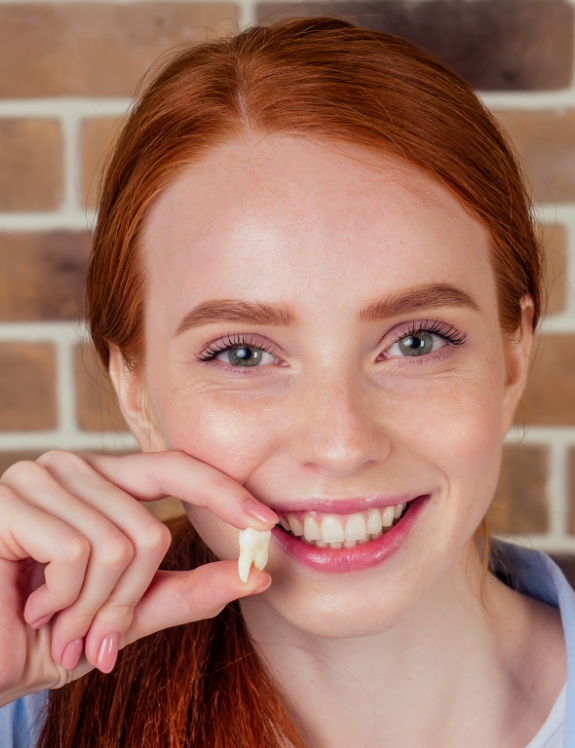 Smiling woman holding an extracted tooth