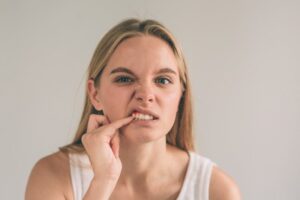 Blonde woman poking at her teeth wondering about her overall health